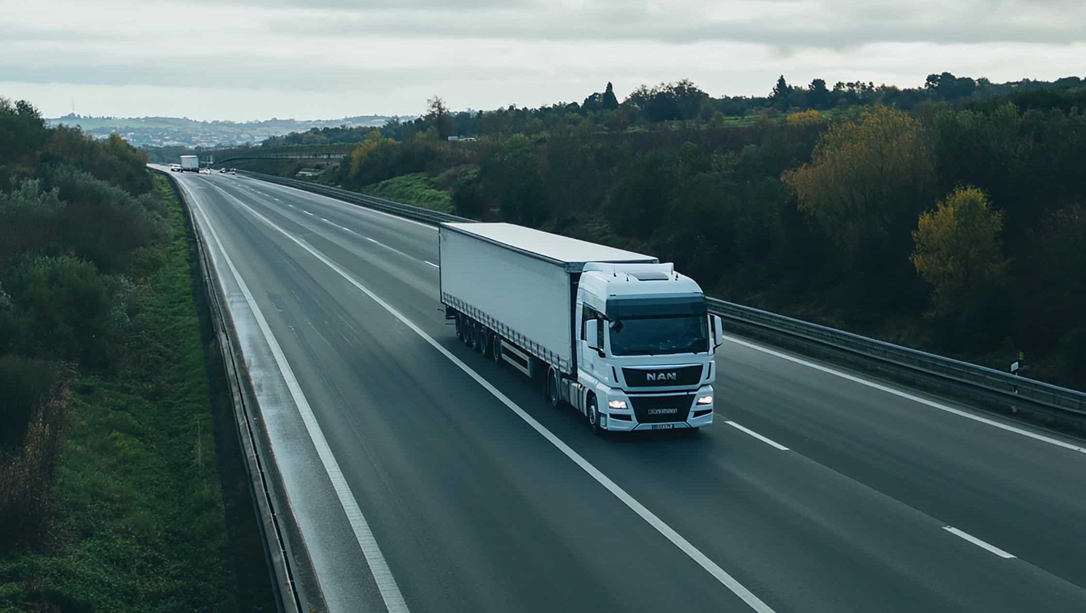 Hvit lastebil på tom motorvei under overskyet himmel.