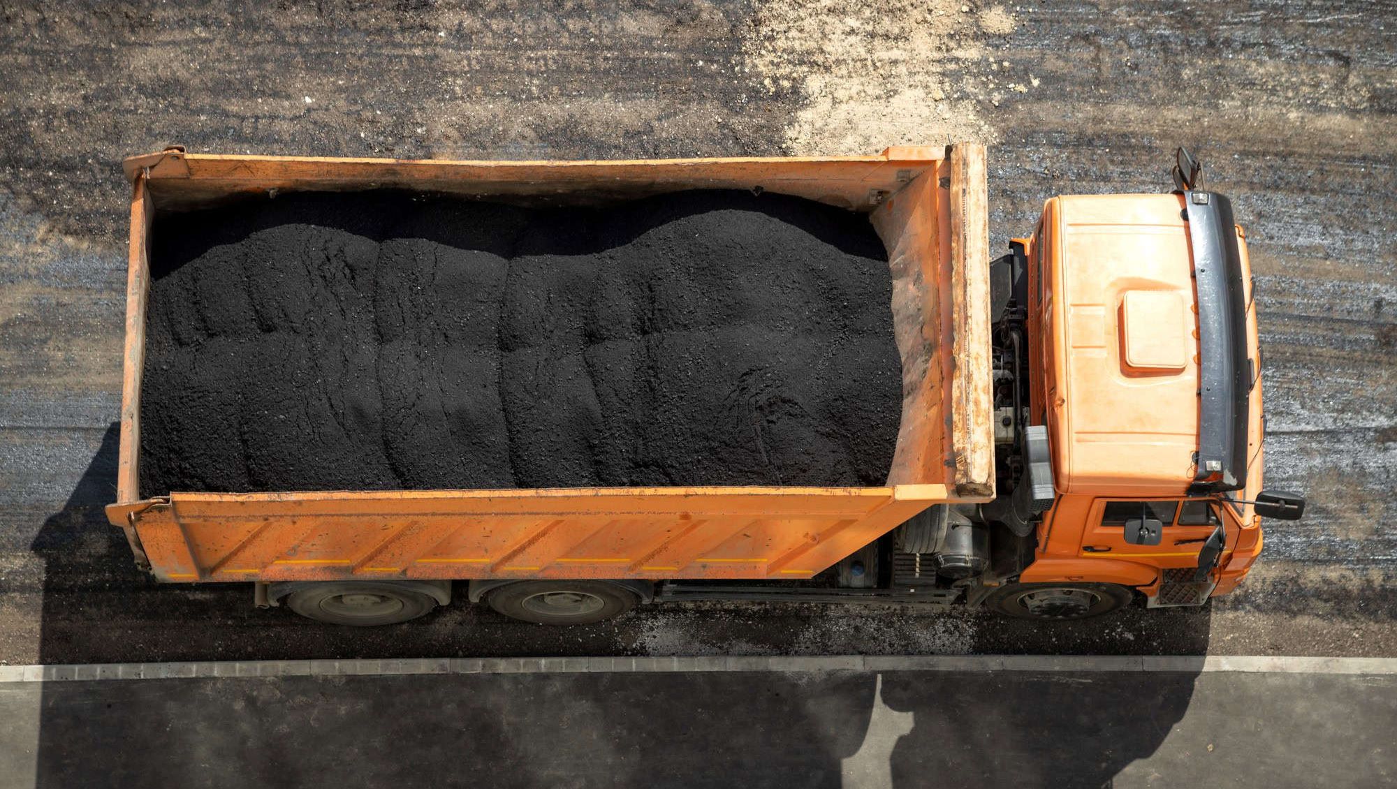 Oransje lastebil sett ovenfra, fylt med svart asfalt.
